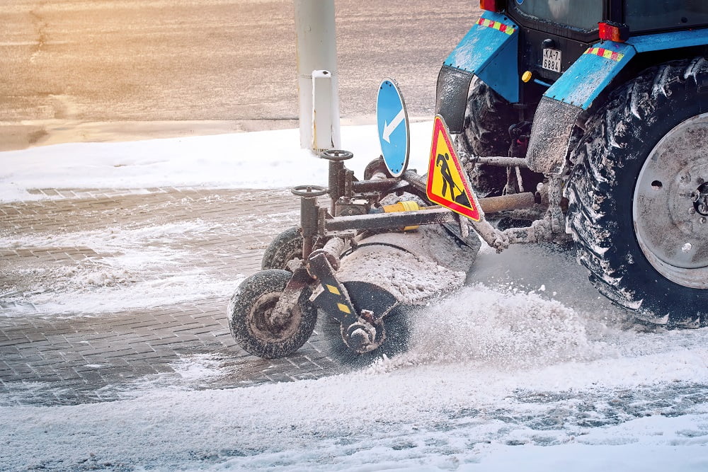 Tractor sweep snow with rotating brush from pedestrian zone, sidewalk snow management during blizzard. Snow plow service remove snow and ice from road, winter road maintenance